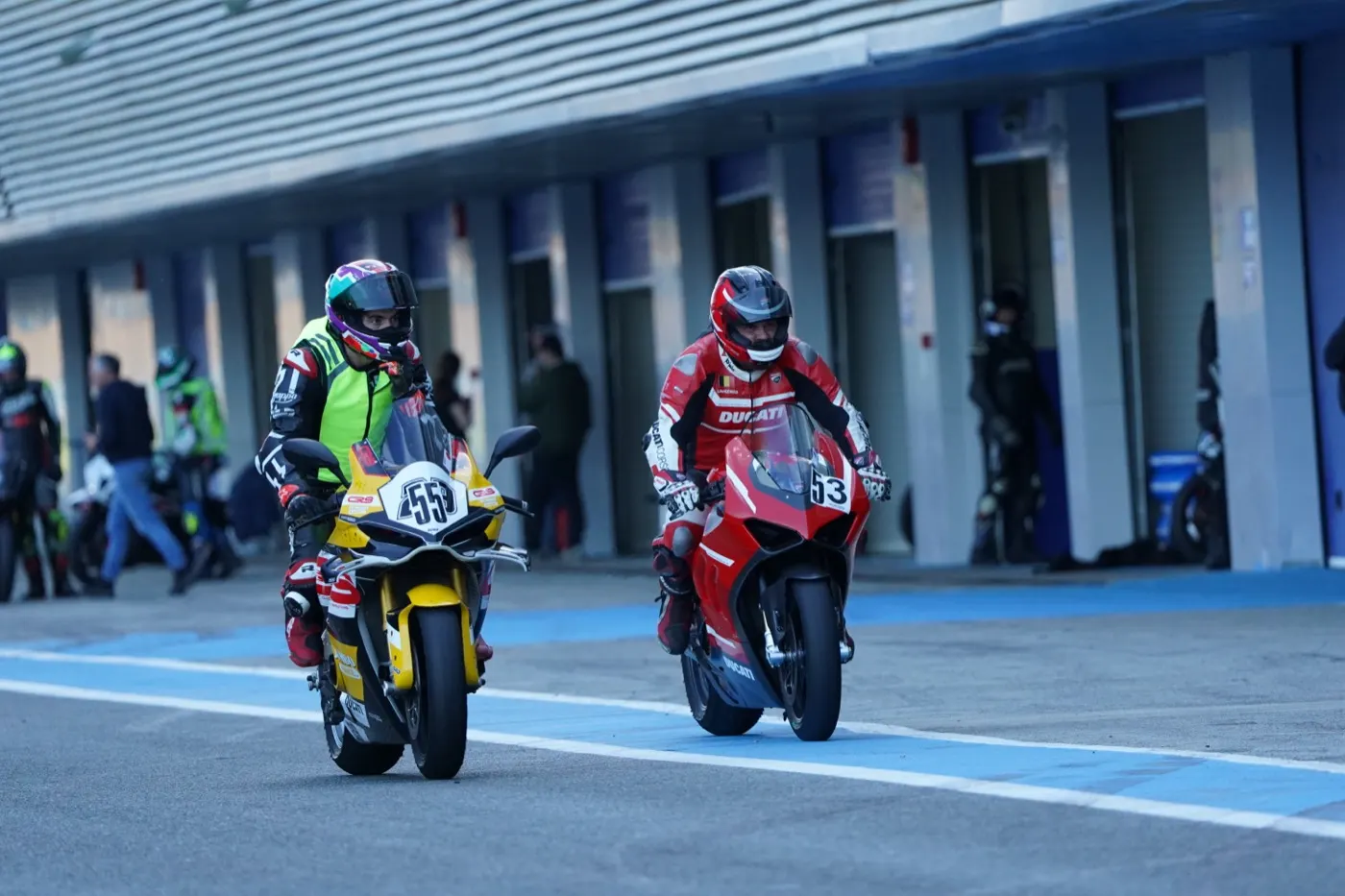 Two riders heading out of the pit lane onto the circuit