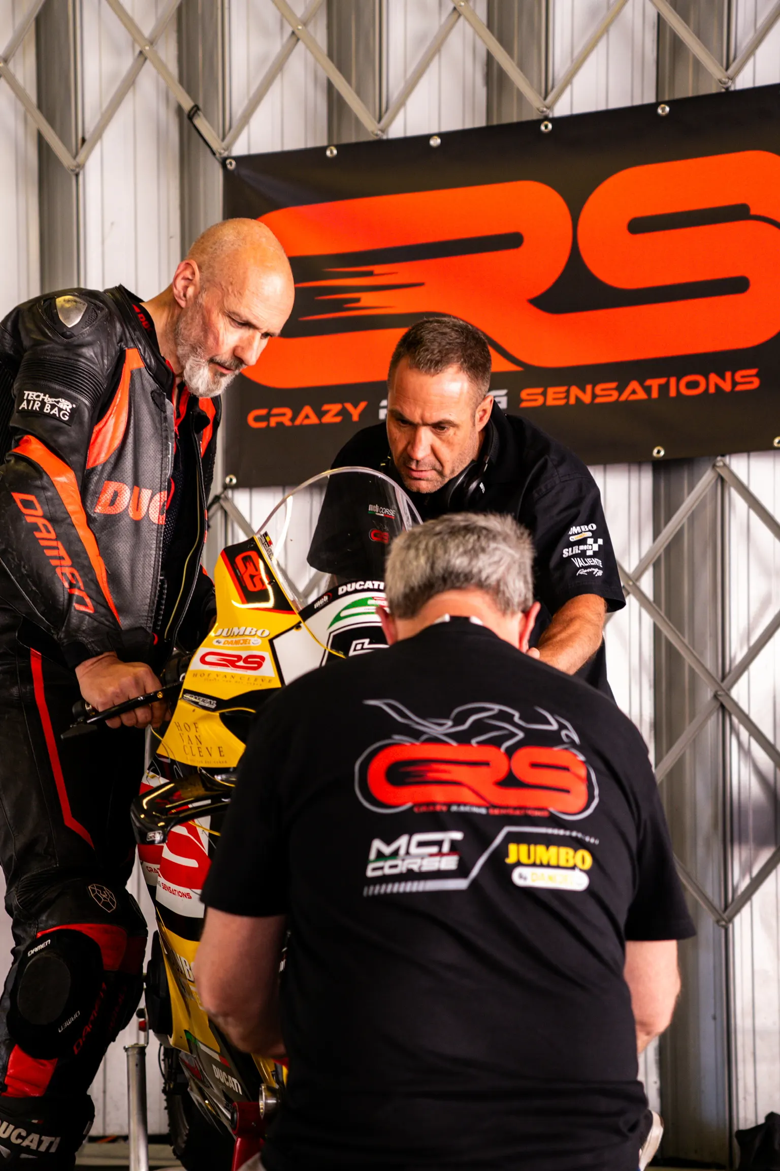 Three riders talking beside a Ducati under the CRS banner